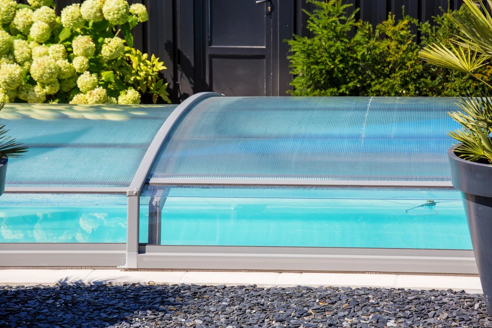Femme se relaxant dans une piscine extérieure, appuyée contre le rebord carrelé, portant lunettes de soleil et maillot de bain noir